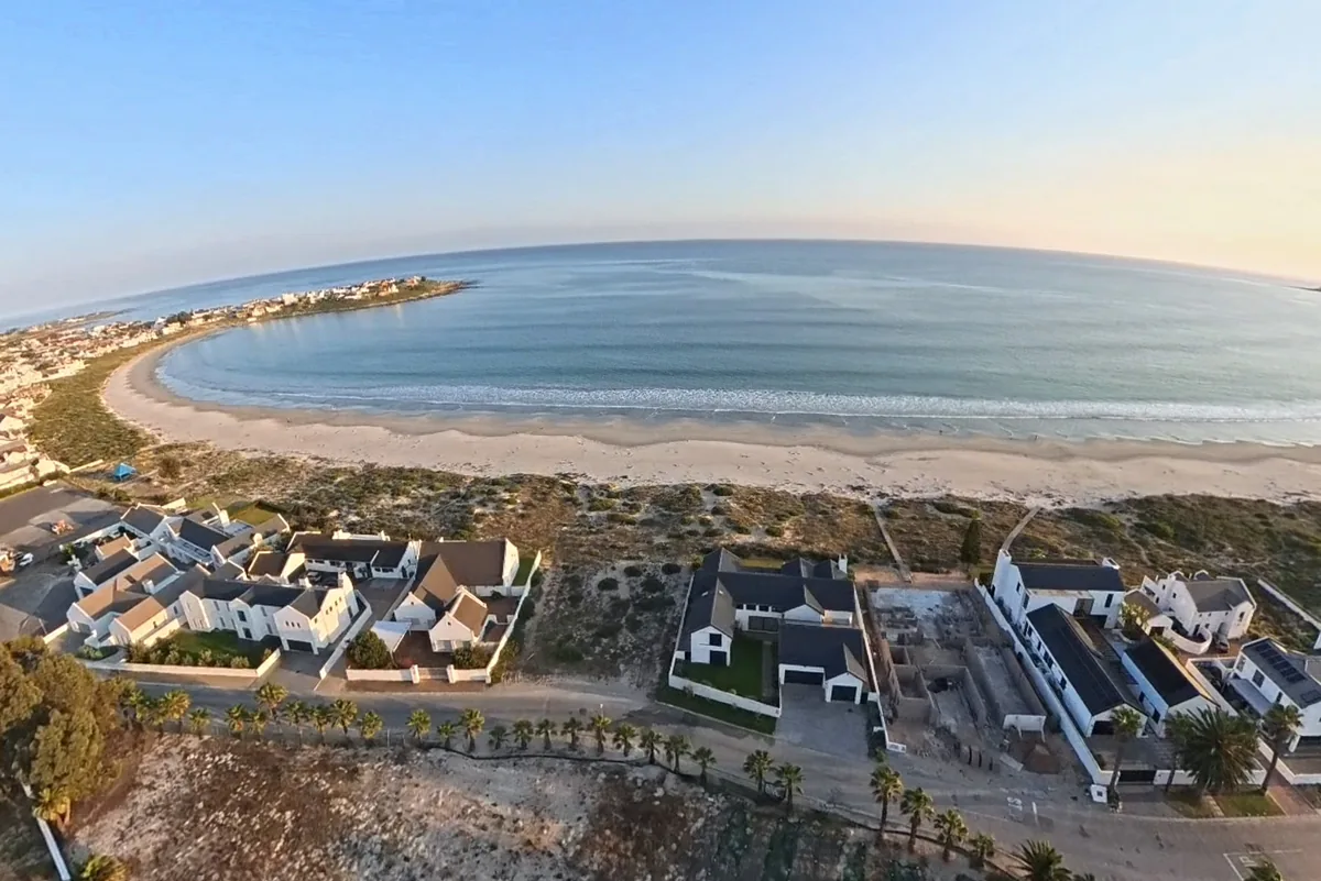 Aerial view of Britannia Bay at dusk: the Golden Mile curve, white West Coast houses and the Atlantic, with Five Fires in the estate below.